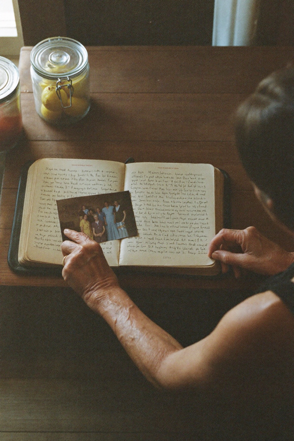 An older woman and her carer leaning over a handwritten recipe book together at a kitchen bench.