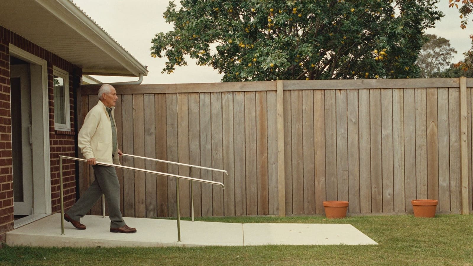 An older man walking up a gentle new concrete ramp to the back door of his home.