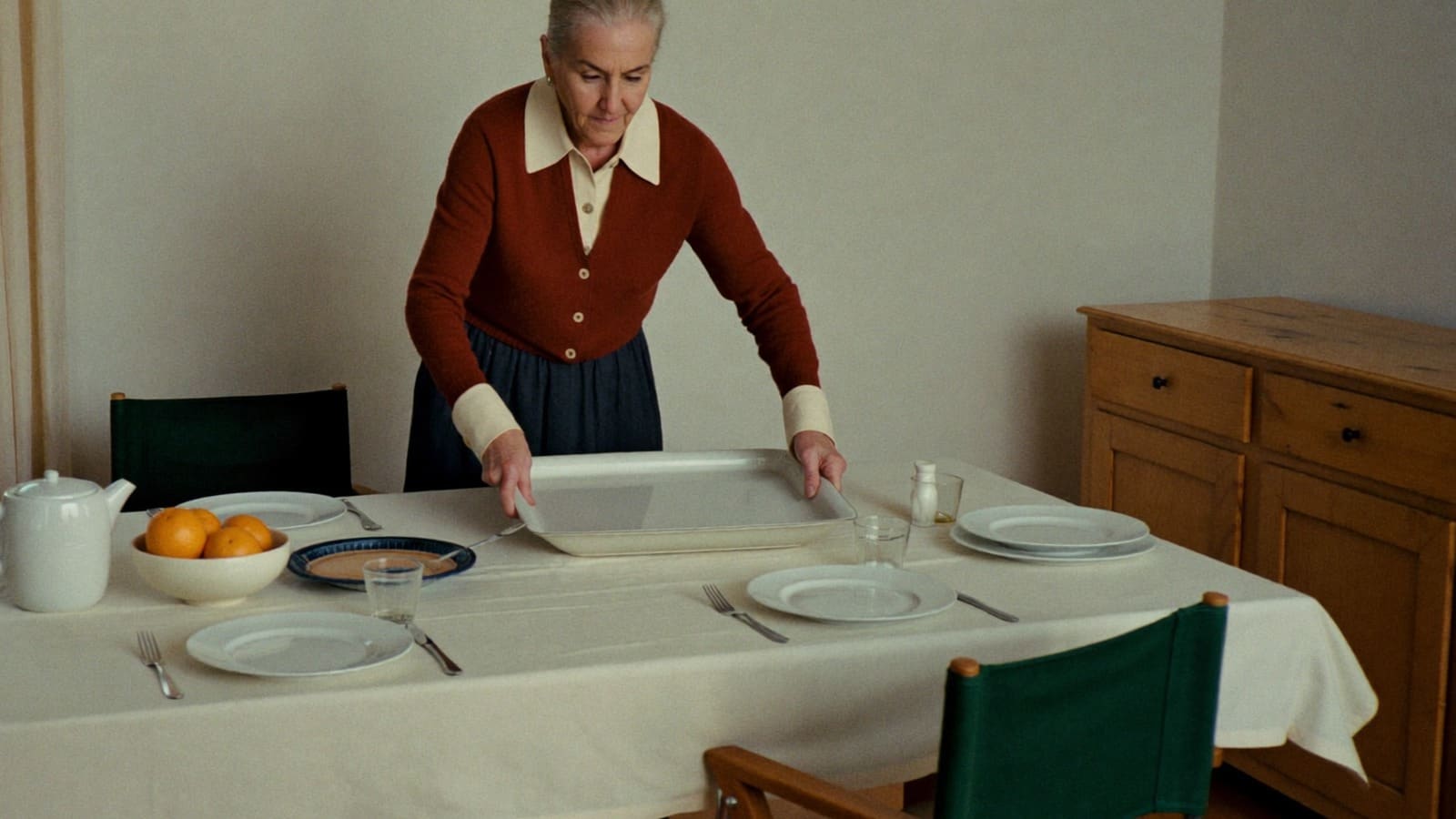 An older woman setting a covered dish down on a table laid for a family meal.