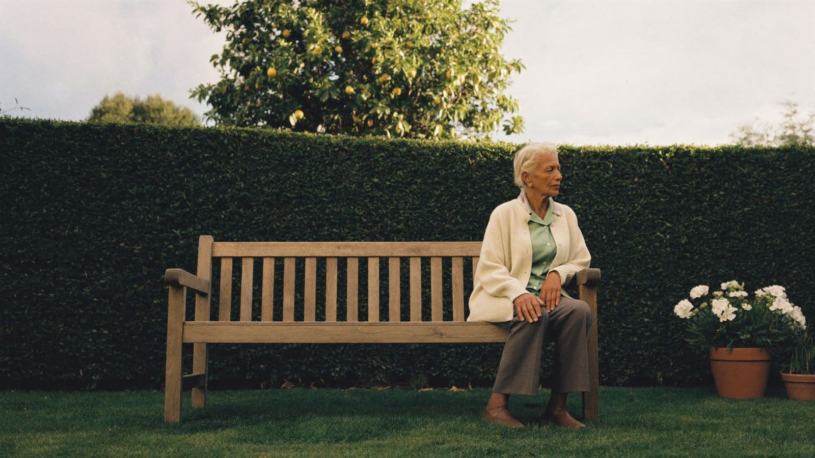 An older woman sitting alone on a timber bench in her back garden, taking a quiet moment.