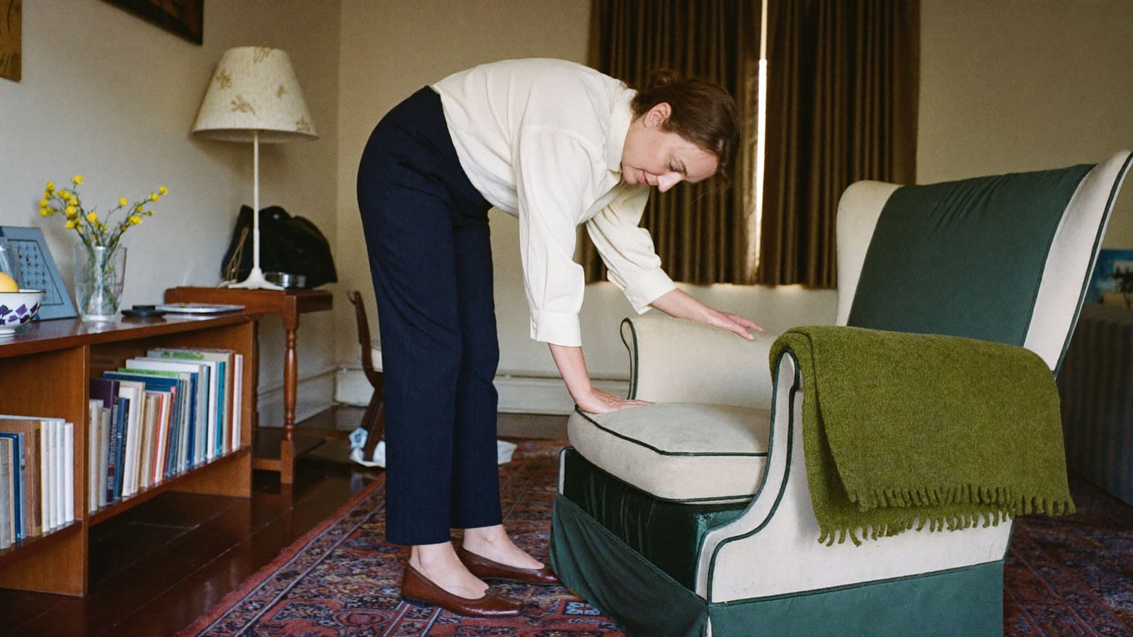 A woman moving a dining chair clear of a walkway while getting her father's living room ready.