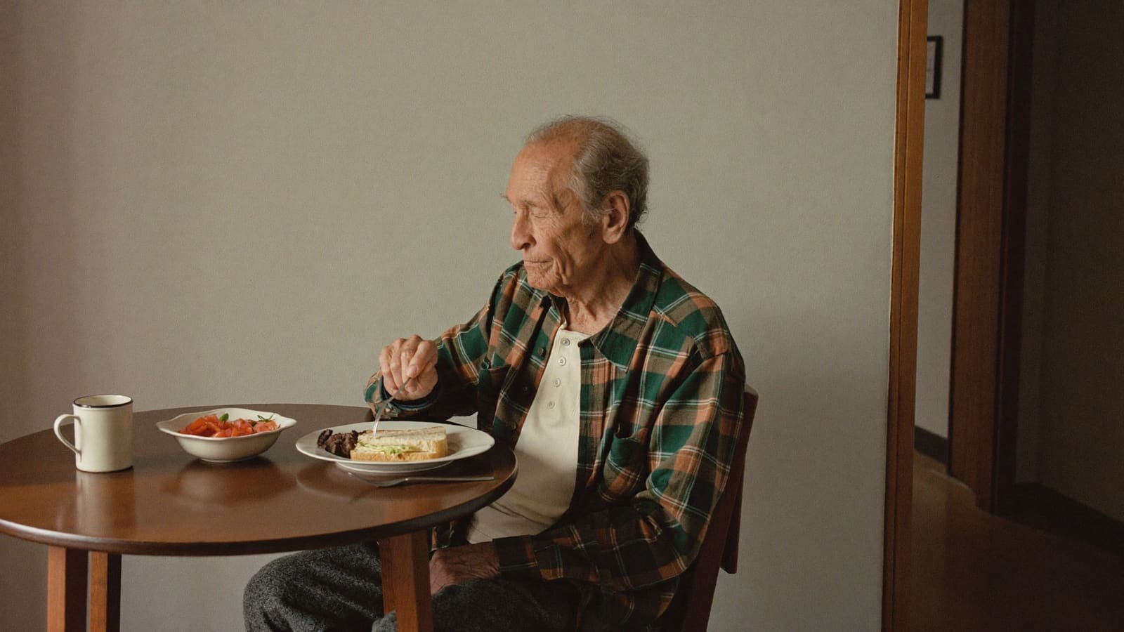 An older man part way through a simple lunch at his own small round kitchen table.