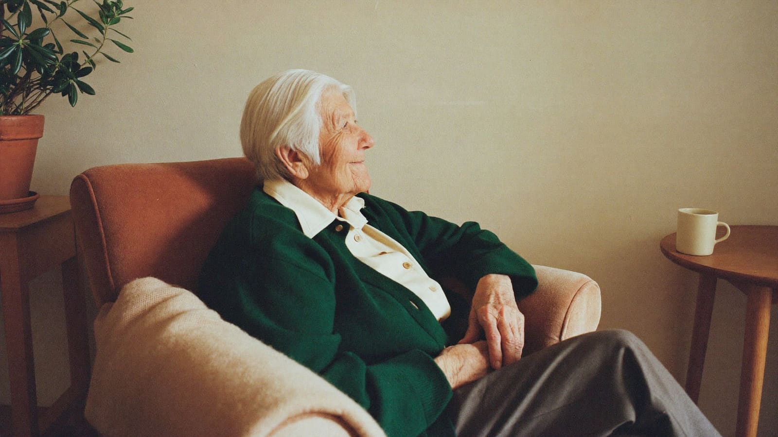 An older woman settled comfortably in her own armchair in a sunlit living room.