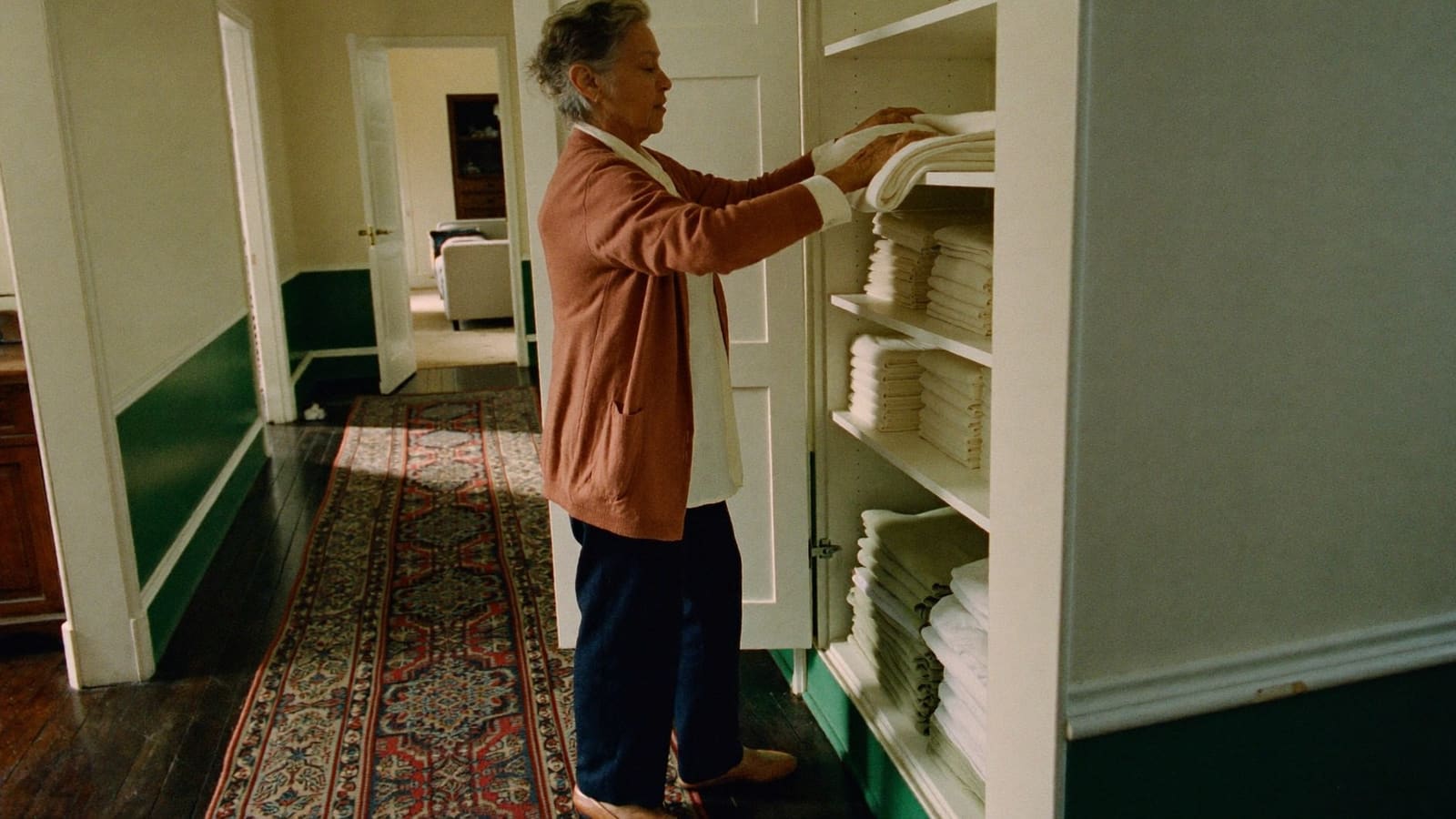 An older woman putting folded towels away in the linen cupboard in her hallway.