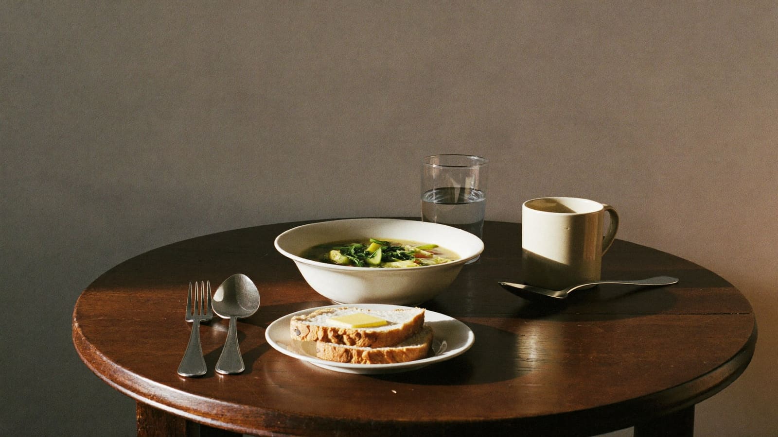 A simple lunch of soup and buttered bread set out on a small round kitchen table.