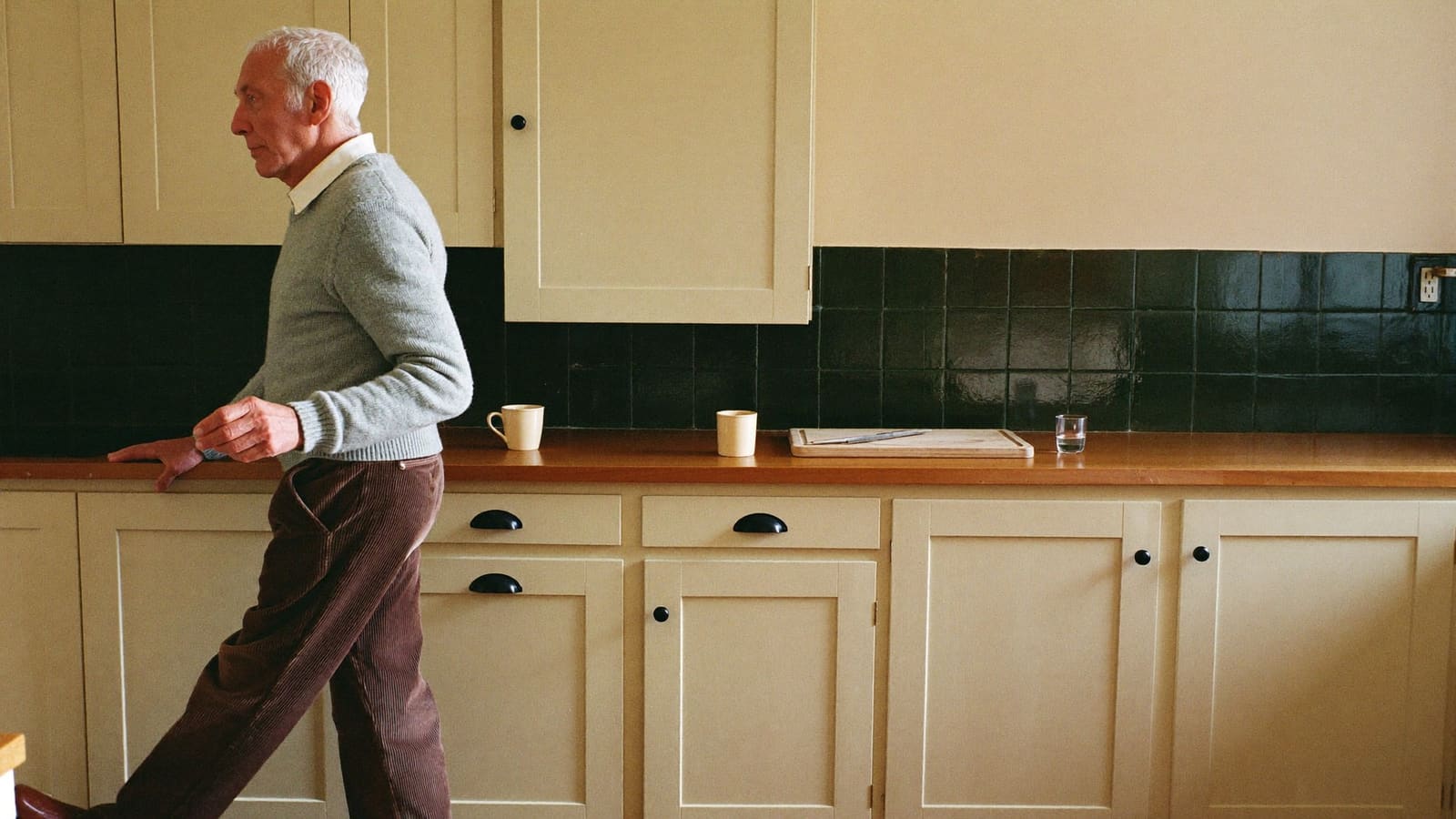 An older man walking slowly along his kitchen bench with one hand trailing the benchtop for steadiness.