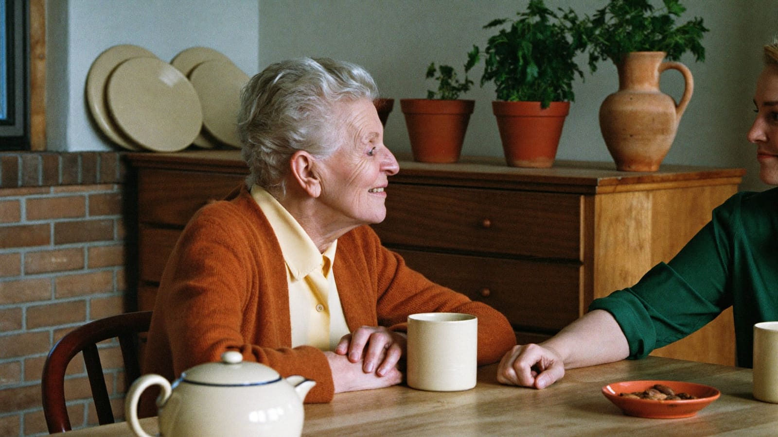 An older woman talking with another woman across her kitchen table over tea.