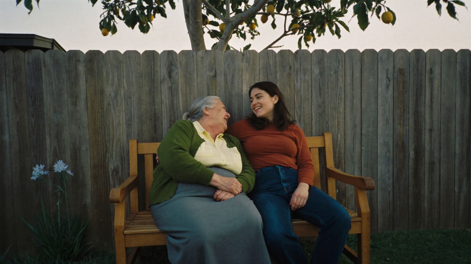 Two women sitting together on a garden bench in a suburban backyard, mid-conversation.