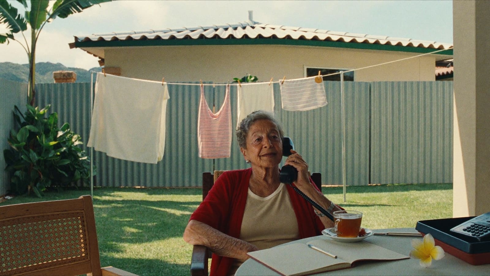 An older woman on her back veranda with a cup of tea, a notepad and the phone within reach.
